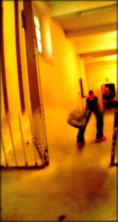 Deux visiteurs de dos dans un couloir sombre ouvert sur une lumière chaude.
